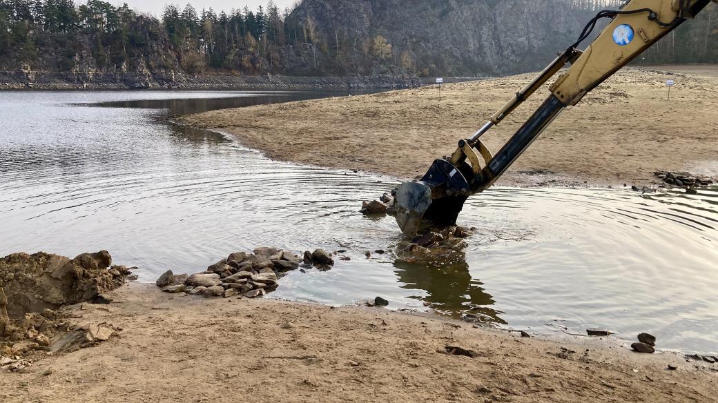 Bagr rozhrnuje cestičku na ostrov, kterou lidé postavili z kamenů