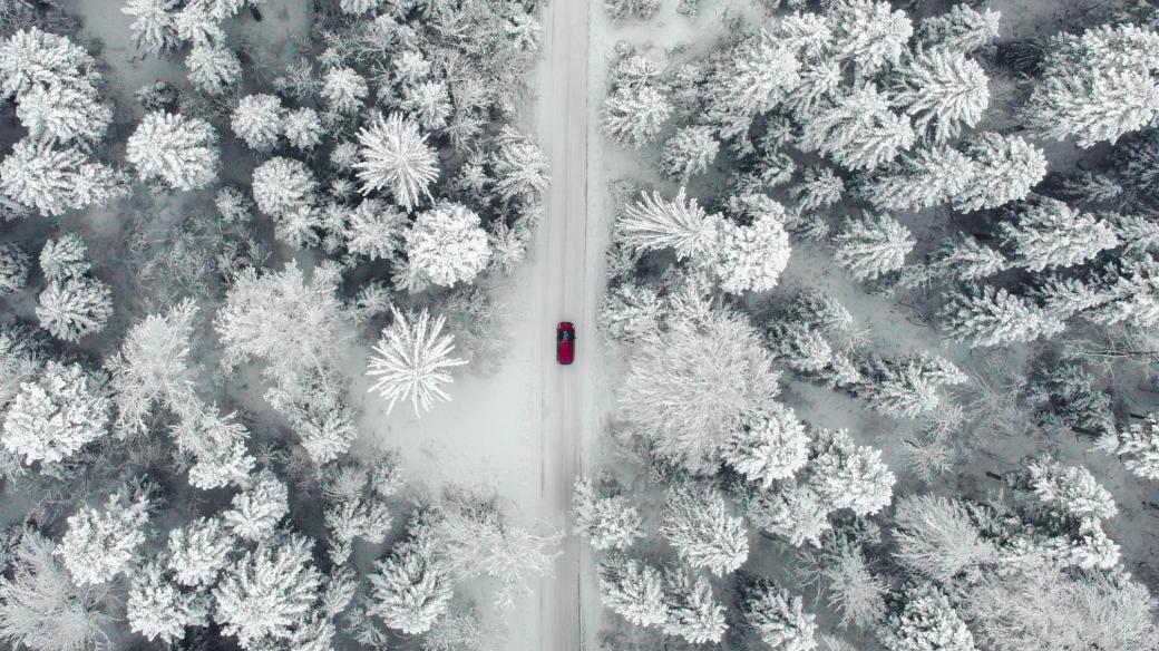 Červené auto jedoucí zasněženou zimní krajinou