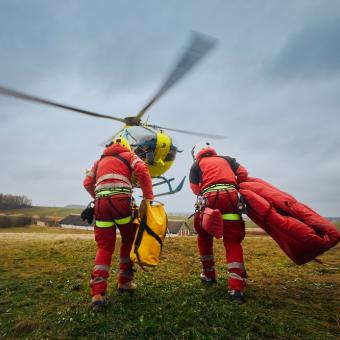 Záchranáři s bezpečnostním postrojem a horolezeckým vybavením běží k vrtulníku záchranné služby
